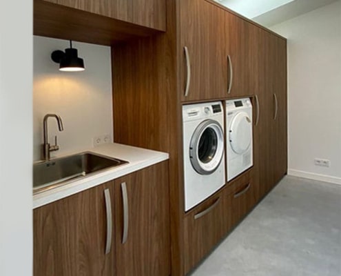 Een wasruimte kast op maat waarin wasmachine en droger netjes zijn weggewerkt, met opbergruimte voor wasmand, strijkplank en schoonmaakspullen.