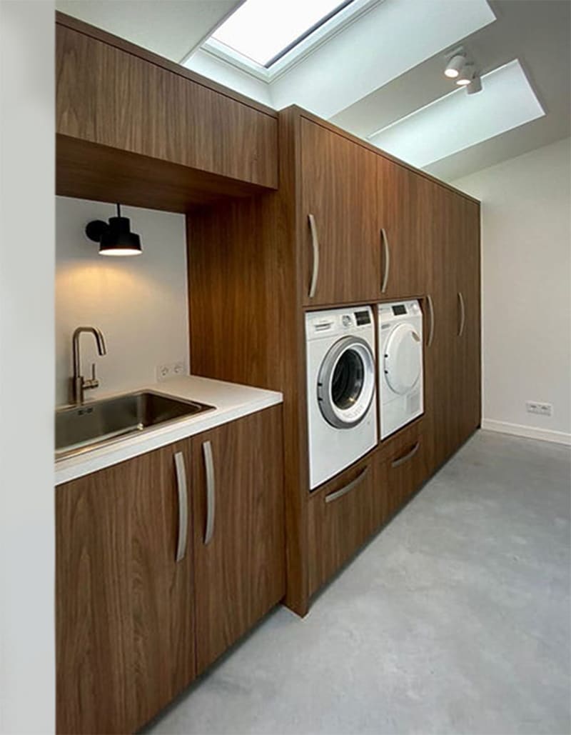 Een wasruimte kast op maat waarin wasmachine en droger netjes zijn weggewerkt, met opbergruimte voor wasmand, strijkplank en schoonmaakspullen.